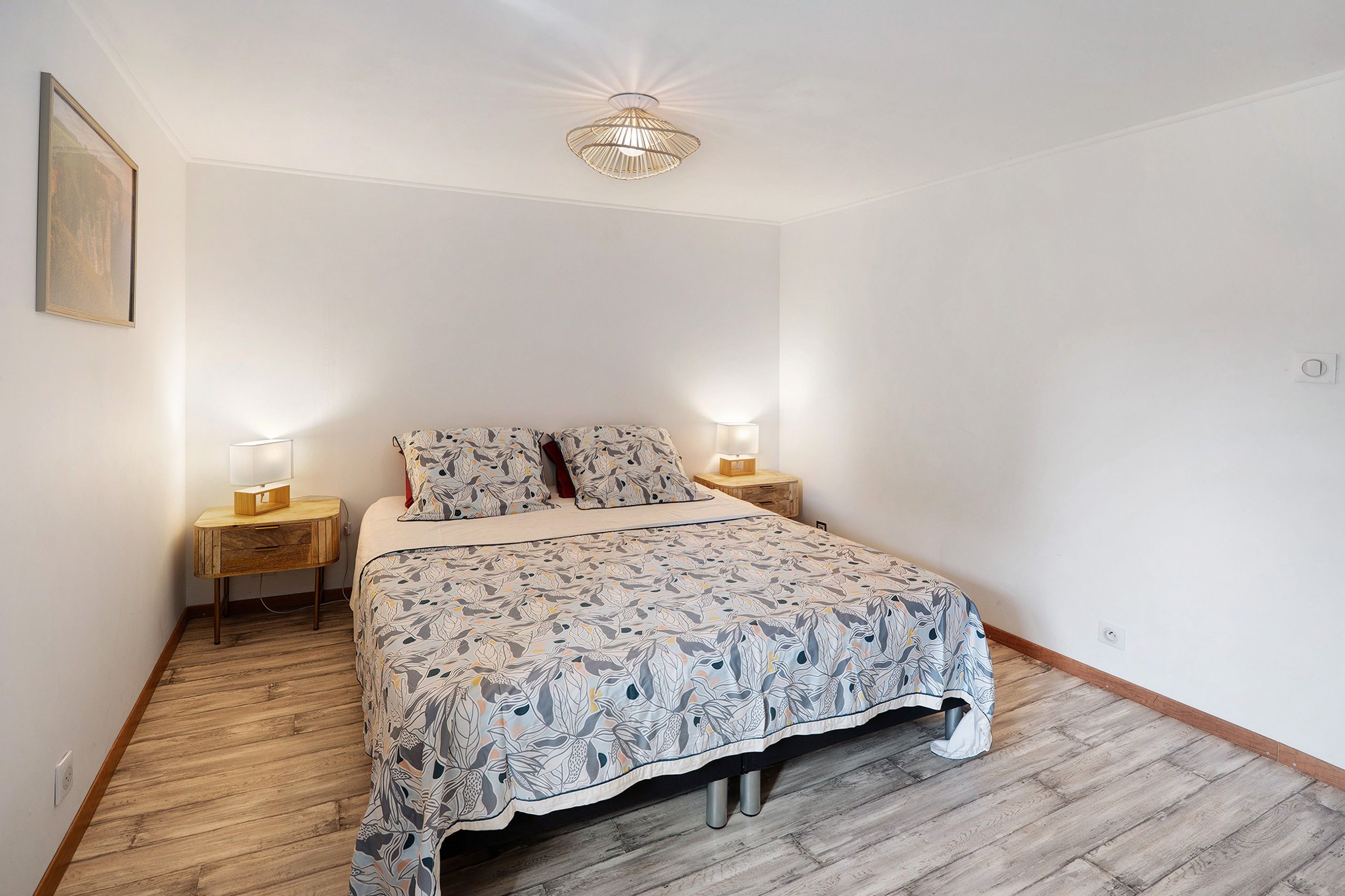 Ein Schlafzimmer mit einem Bett, zwei Nachttischen, einer Wandlampe und einem gerahmten Bild.