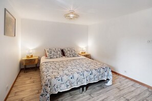 Un dormitorio con una cama, dos mesitas de noche, un buró, una lámpara de pared e imagen enmarcada.