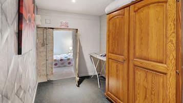 Ein Zimmer mit einem hölzernen Kleiderschrank, einem Bett mit farbenfroher Bettdecke und einem kleinen Tisch mit Lampe.