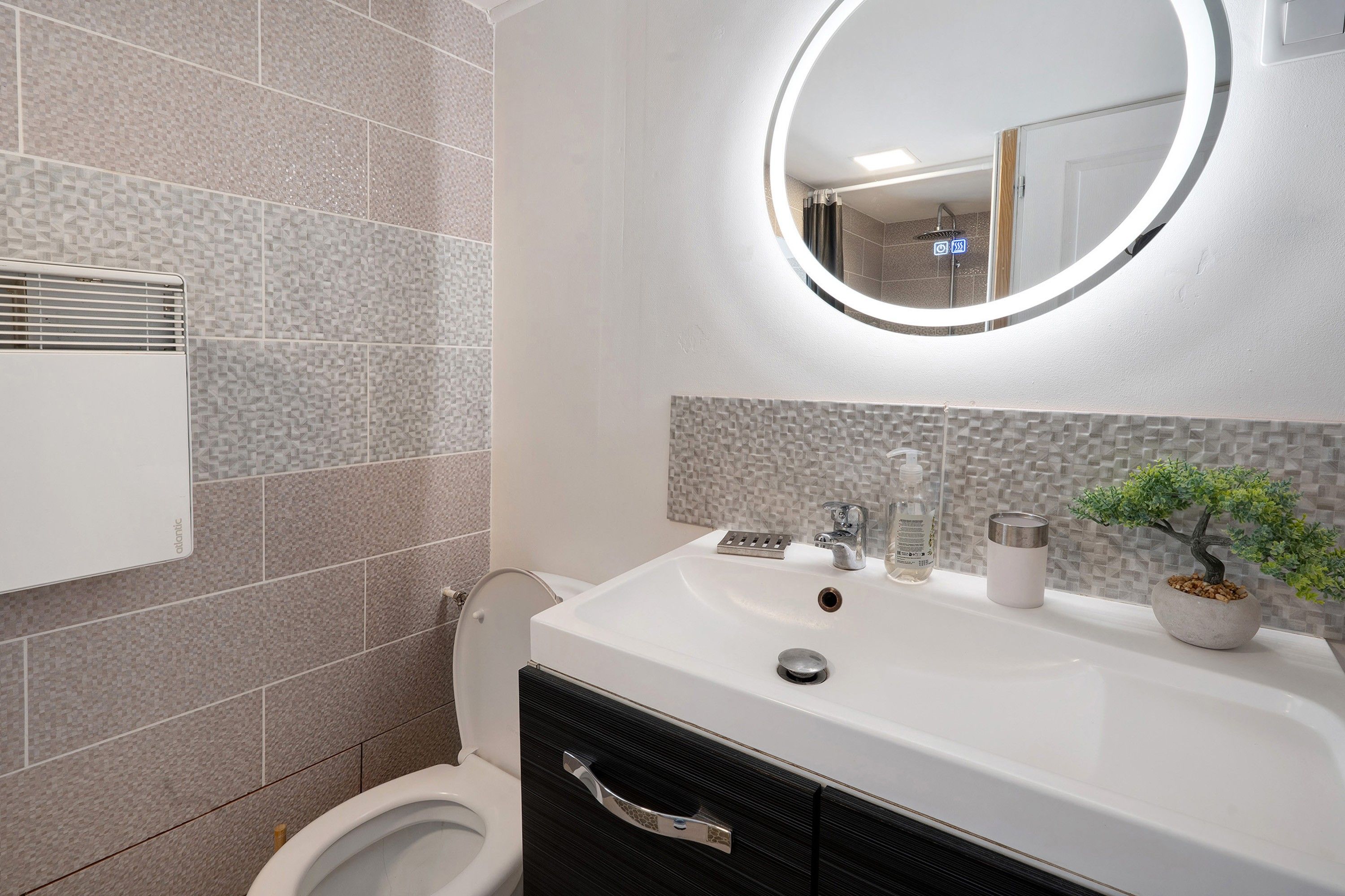 A modern bathroom with a round mirror, a white sink, and a toilet.