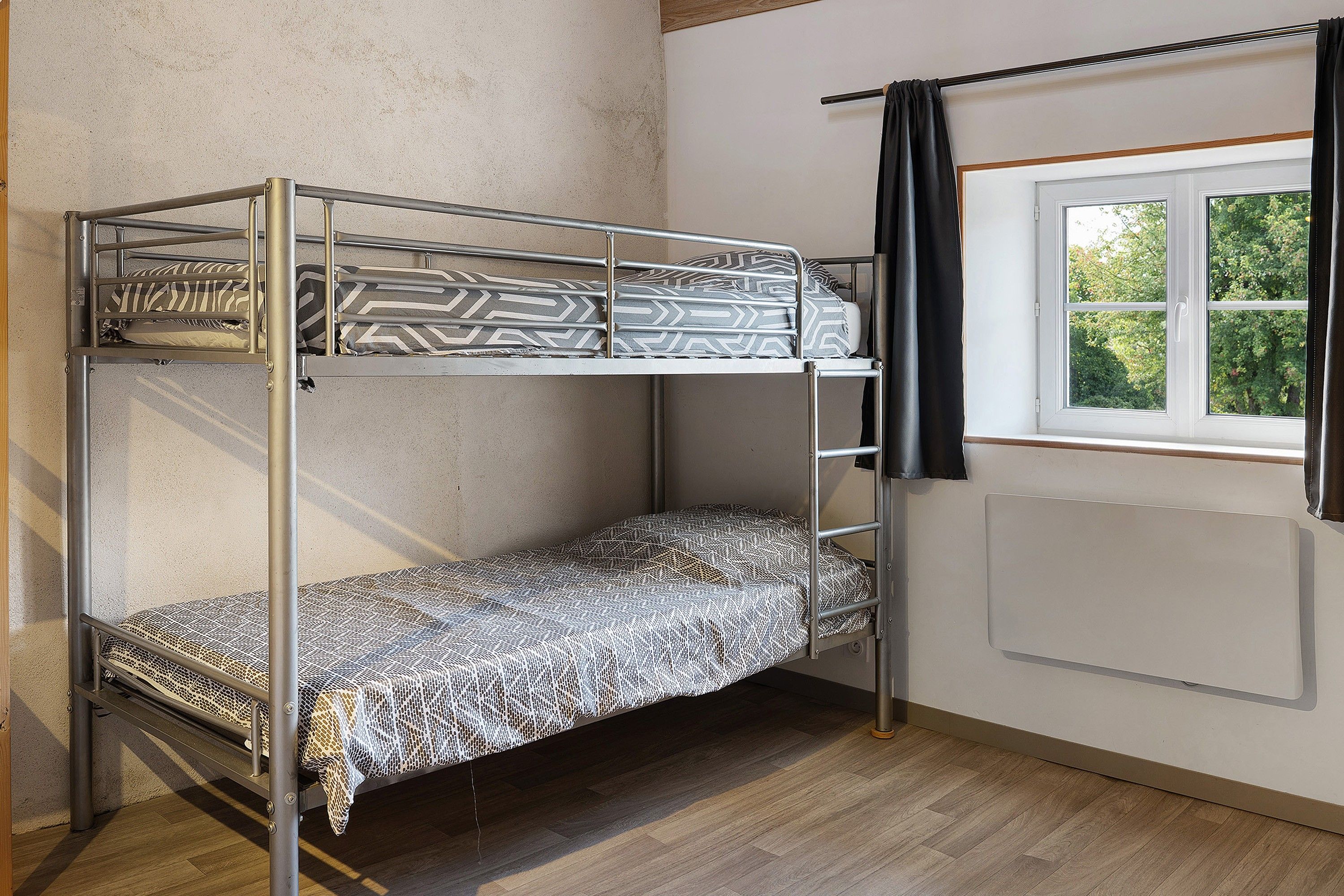 Un lit superposé avec une literie à motifs, une fenêtre avec des rideaux et un radiateur.