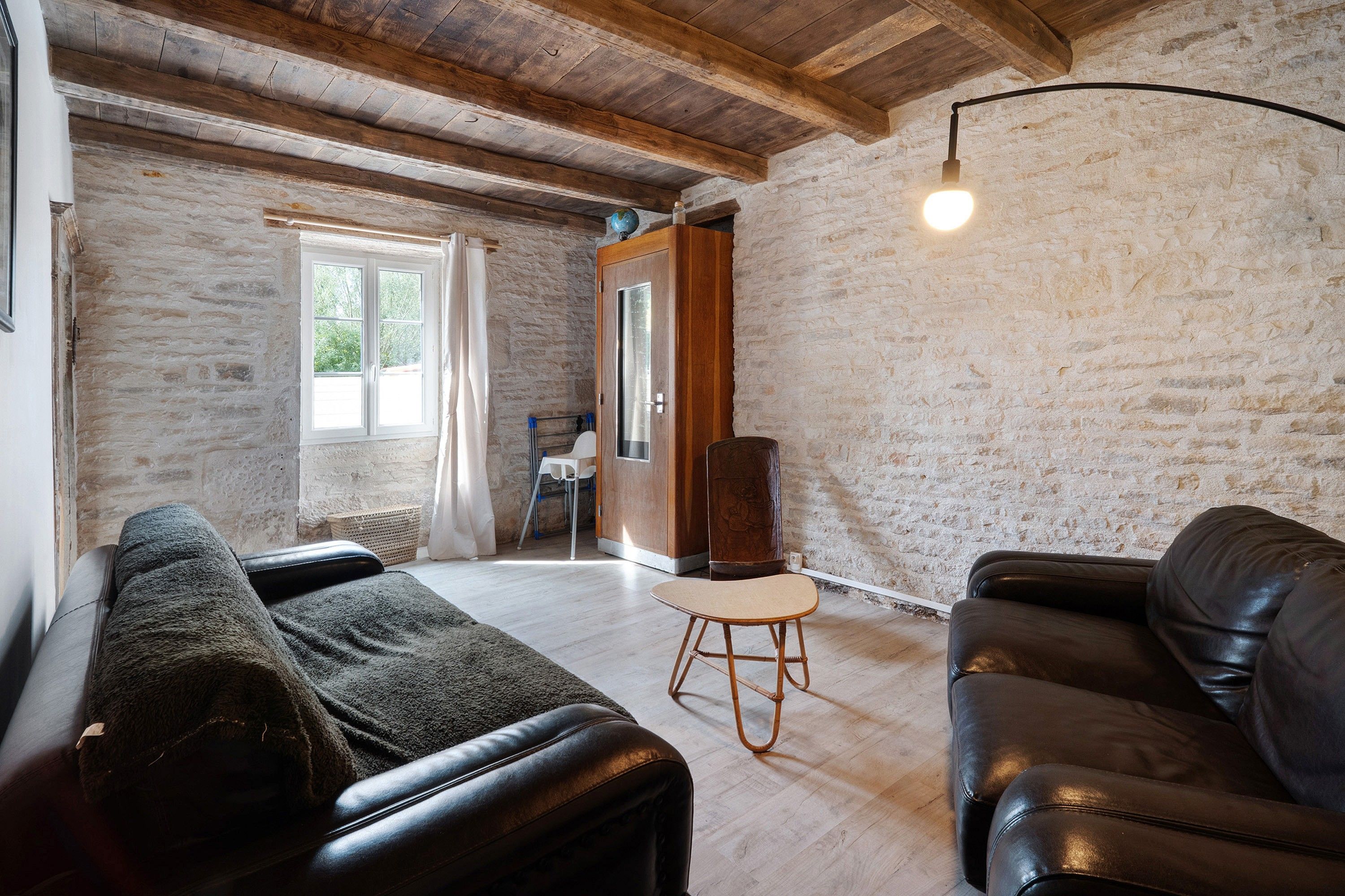 Ein gemütliches Wohnzimmer mit Steinwand, Holzboden und einer schwarzen Ledersofa, einem Holzstuhl und einer Stehlampe.