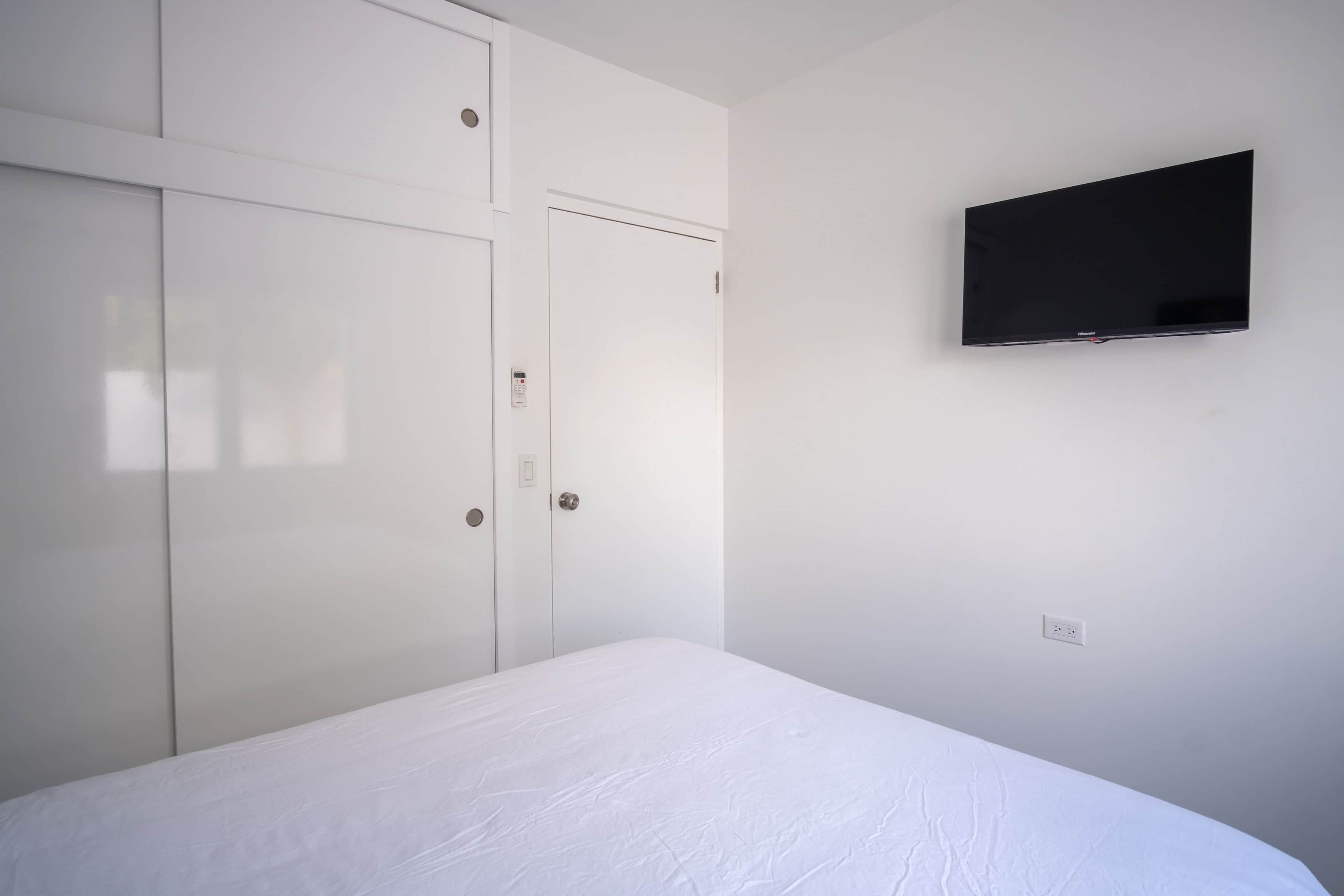 Een slaapkamer met een bed, een kledingkast, een aan de muur bevestigde televisie en een stopcontact.