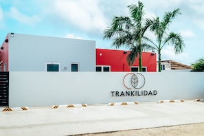 Un edificio con fachada blanca y roja, una palmera y un letrero que dice 'TRANKILIDAD'.