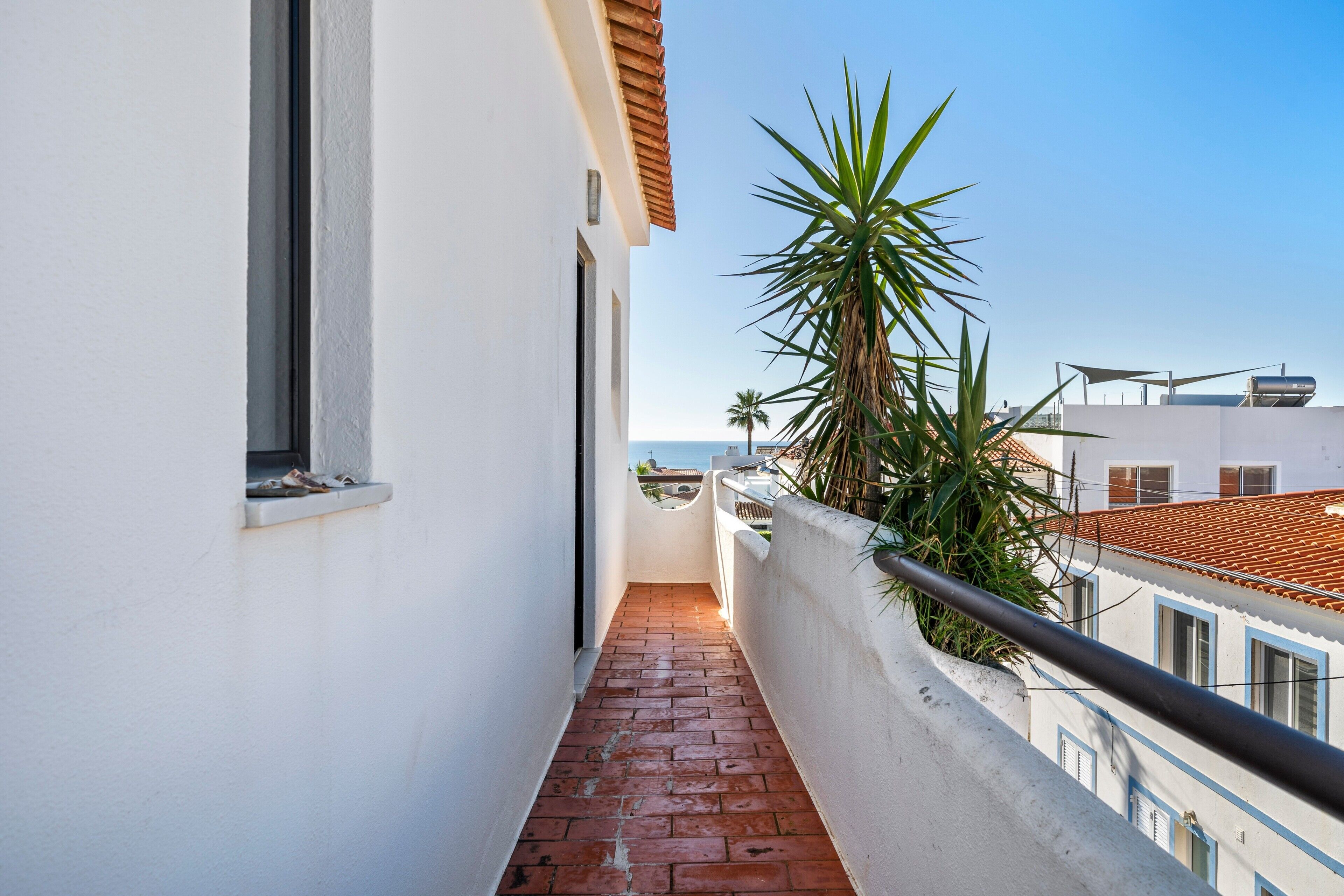 A narrow balcony with a red brick floor, white walls, and a view of the sea.