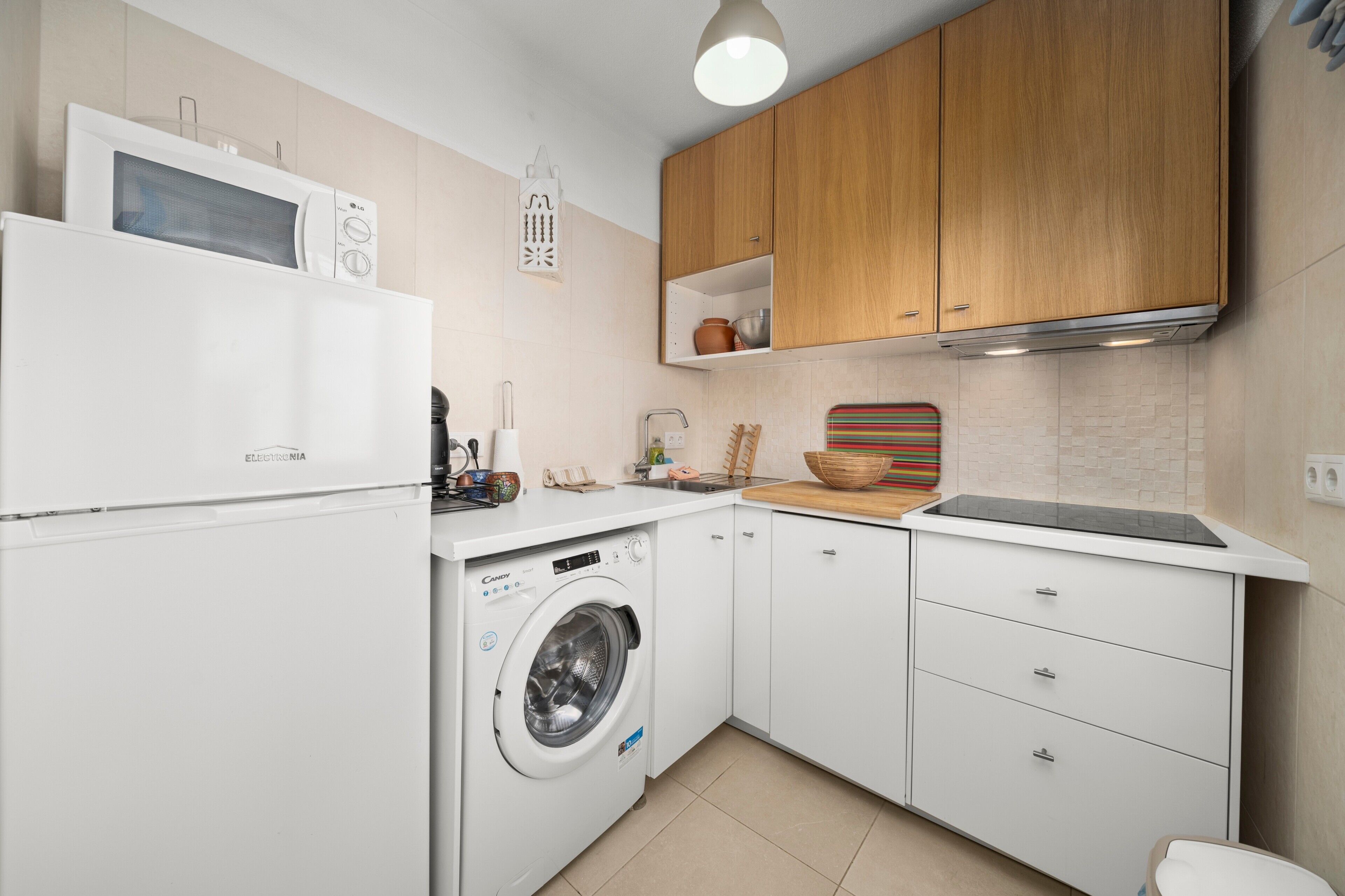 A compact kitchen with a microwave, washing machine, wooden cabinets, and a countertop with various kitchen items.