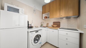 Una cocina compacta con microondas, lavadora, armarios de madera y una encimera con diversos utensilios de cocina.