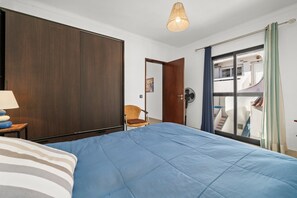 Ein Schlafzimmer mit Bett, Stuhl, Kleiderschrank, Ventilator und Blick auf einen Balkon.