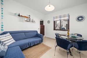 A living room with a blue sofa, a dining table with chairs, a hanging light fixture, and a wall-mounted mirror. - Casa Tété in Benagil – Authentic Algarve Charm Steps from the Beach (benagil)