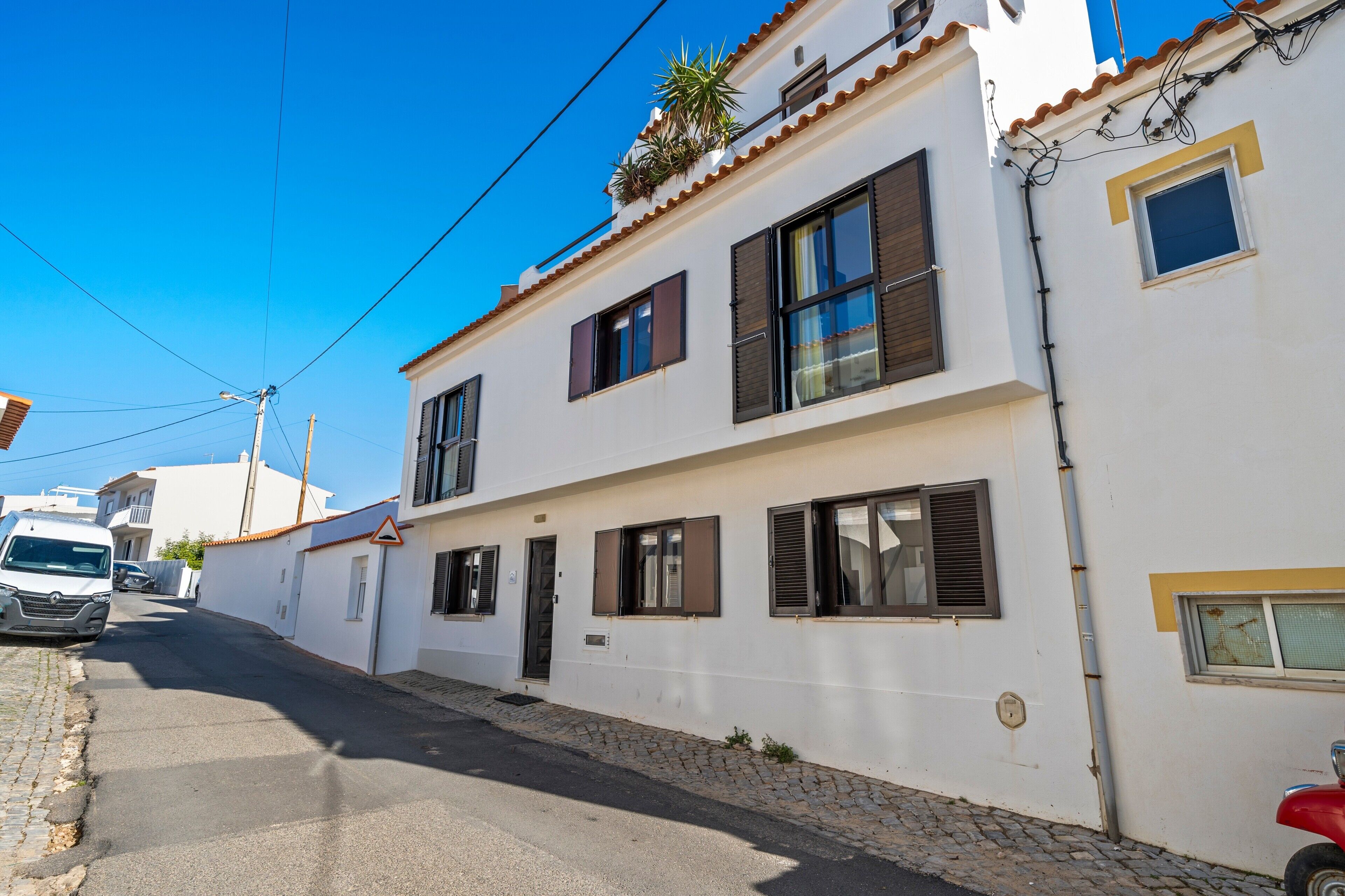 A two-story building with a white facade, multiple windows with shutters, and a cobblestone street.