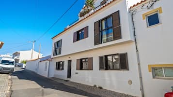 A two-story building with a white facade, multiple windows with shutters, and a cobblestone street.