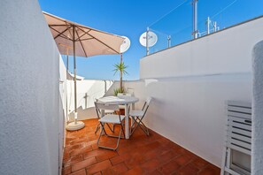 Eine Terrasse mit einem weißen Tisch, Stühlen und einem beigen Sonnenschirm.