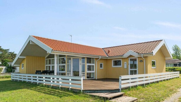 A yellow building with a red-tiled roof, a covered porch, and a white fence. - 5 Star Holiday Home in Knebel (Knebel)
