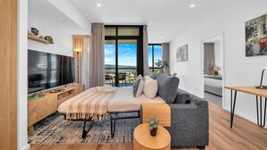 A modern living room with a large bed, a TV, and a view of the outdoors. - Luxe on Franklin | Car Park, Lap Pool, Sauna, BBQ (Adelaide)