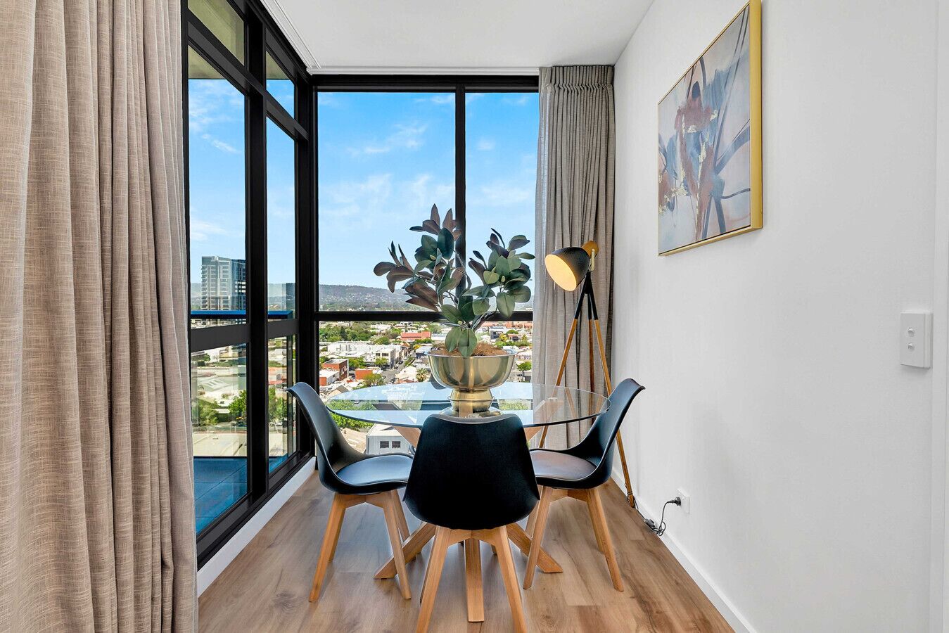 A modern room with a large window, a dining table with chairs, a potted plant, and a floor lamp.