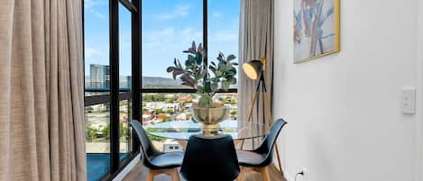 A modern room with a large window, a dining table with chairs, a potted plant, and a floor lamp.