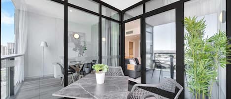 Un balcon moderne avec une paroi en verre, une table à manger avec des chaises et une plante en pot.