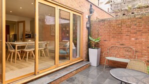 A patio area with a table and chairs, a white planter, and a metal bench. - Host & Stay | Aurora (Deal)