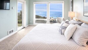 Un dormitorio con una cama grande, televisión y vista al océano a través de un ventanal corredero.