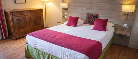 A hotel room with a large bed, wooden headboard, bedside lamps, a dresser, and a framed picture on the wall.