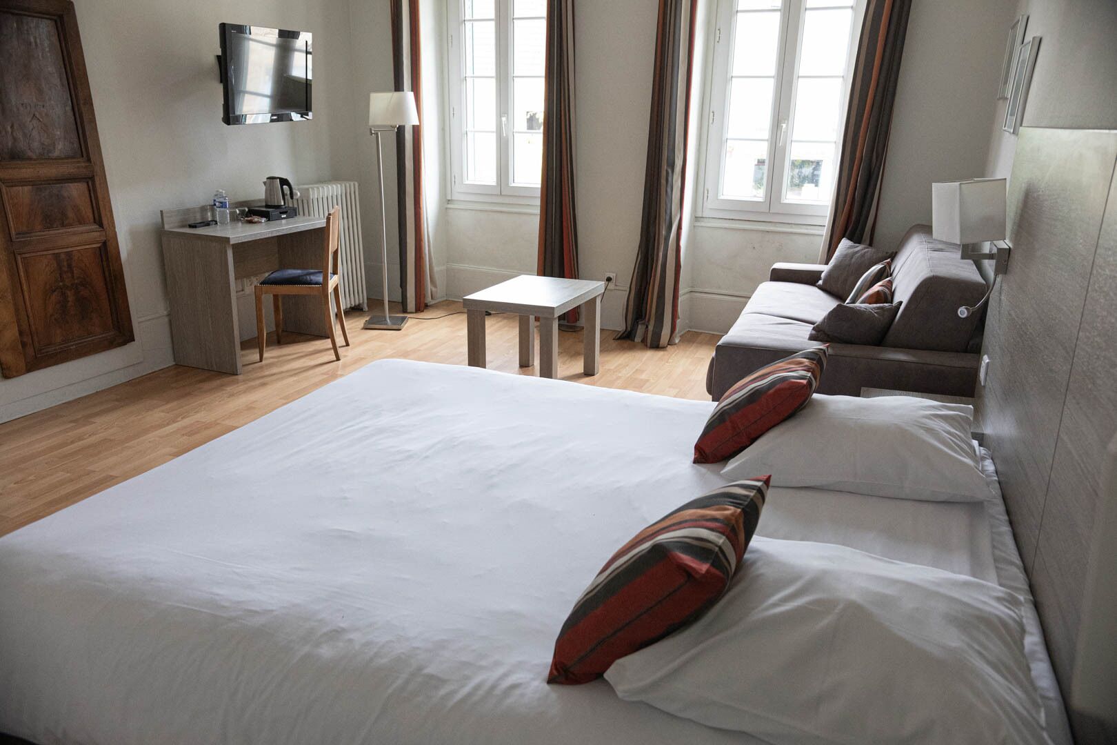 Quarto de hotel com uma cama grande, uma escrivaninha, uma cadeira, uma mesa e um sofá.