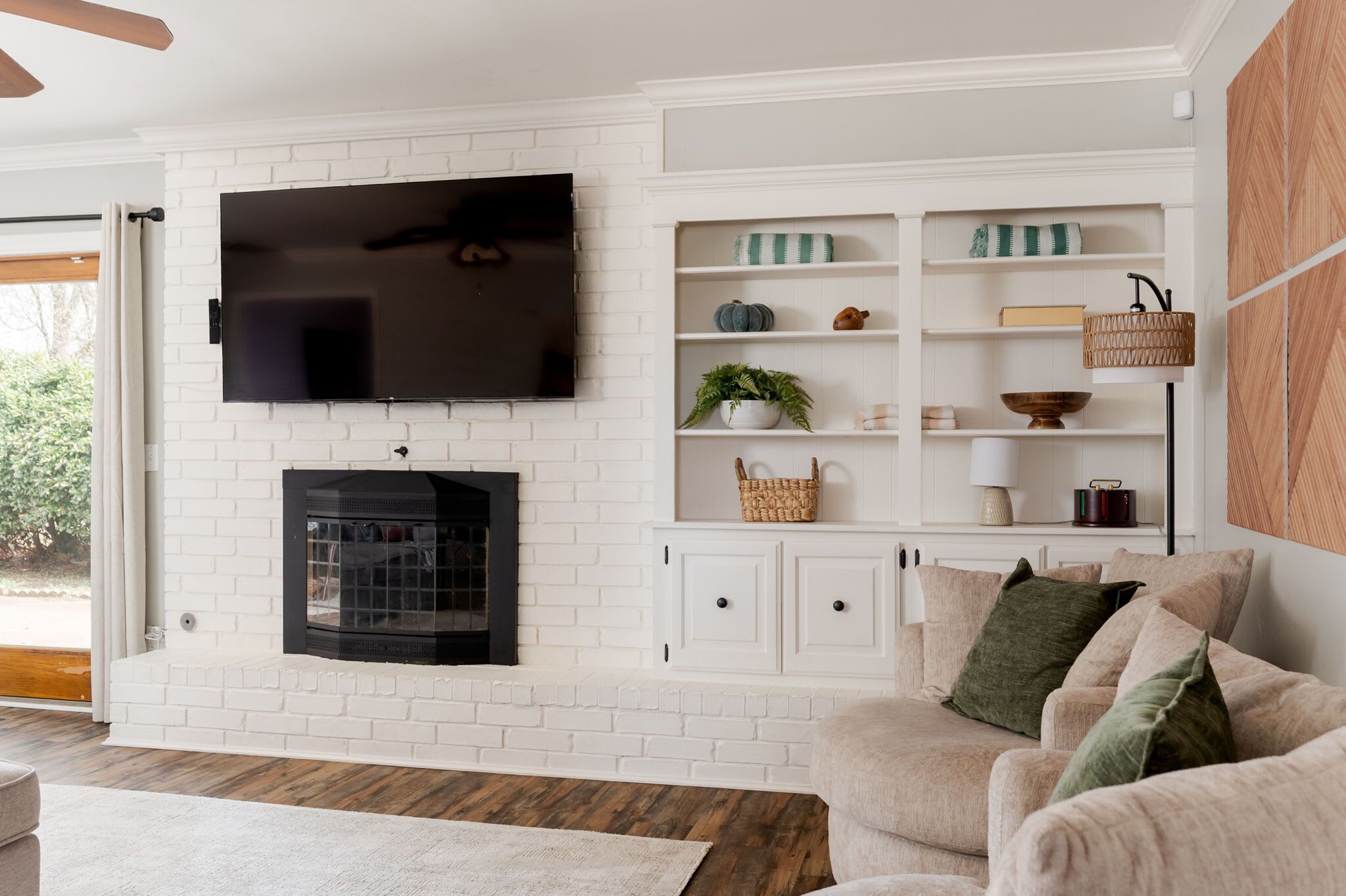 A living room with a white brick fireplace, a flat-screen TV mounted above it, and a built-in shelving unit with decorative items.