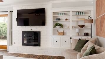 A living room with a white brick fireplace, a flat-screen TV mounted above it, and a built-in shelving unit with decorative items.