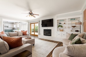 A modern living room with a fireplace, white brick walls, and a large flat-screen TV mounted above it.