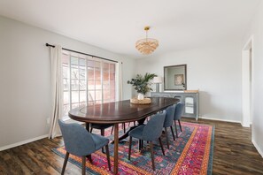 A dining area with a dark wooden table, six chairs, a colorful rug, and a chandelier.