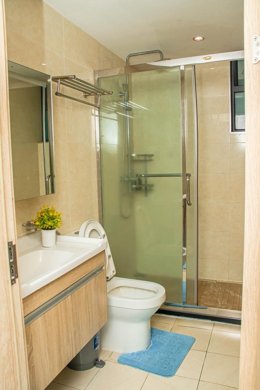 Een badkamer met een douche met glazen wand, een wit toilet, een wastafel met spiegel en een kleine plant in pot.