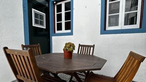 Un patio con una mesa redonda de madera y cuatro sillas, una planta en maceta y piso de baldosas.
