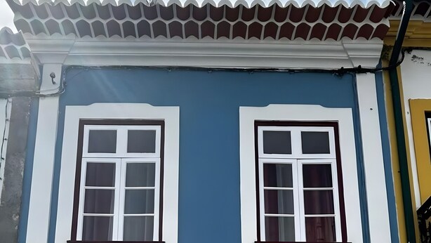 Un edificio de dos pisos con ventanas de marco blanco, fachada azul y puertas numeradas.