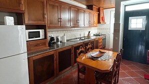 Una cocina con armarios de madera, un refrigerador blanco, una mesa de comedor con sillas y piso de baldosas.