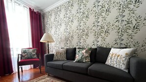 Un salón con un sofá gris oscuro, cojines con estampado floral, alfombra con diseño rojo y beige, una silla roja y una lámpara de pie.