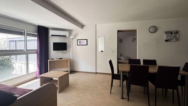 A modern room with a bed, a TV, a desk, and a dining area with chairs. - Apartment in Vernet-les-bains With Pool (Vernet-les-Bains)