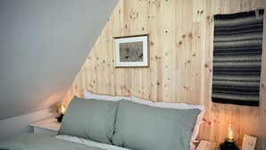 A bedroom with a sloped ceiling, a bed with green bedding, a nightstand with a lamp, and a framed picture on the wall.