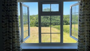 A room with a large window offering a view of a grassy field and trees.
