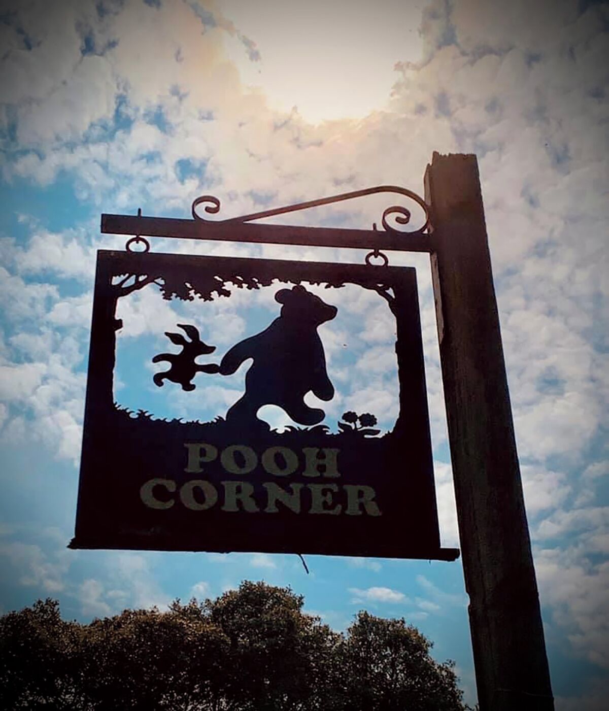 A sign with a bear silhouette and the text "POOH CORNER" against a sky with clouds.
