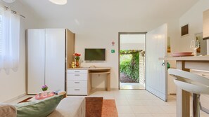 A modern hotel room with a desk, a television, a wardrobe, and a view of greenery outside.
