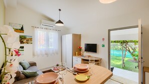 Un comedor con una mesa dispuesta para cuatro, un televisor en la pared y vistas a un jardín por una puerta abierta.