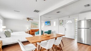 A modern, well-lit room with a wooden dining table, white chairs, a bed with white bedding, a ceiling fan, and a stainless steel refrigerator. - ☀️ Pet Friendly - Entire Property - The Bungalows ☀️ (Treasure Island)