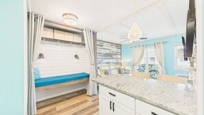 Une cuisine compacte dotée d’un plan de travail en granit, d’un banc intégré avec des coussins et offrant une vue sur les vélos garés à l’extérieur.