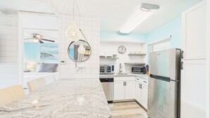 Une cuisine moderne dotée de plans de travail en granit, d’appareils électroménagers en acier inoxydable et d’un coin repas avec une table et des chaises blanches.