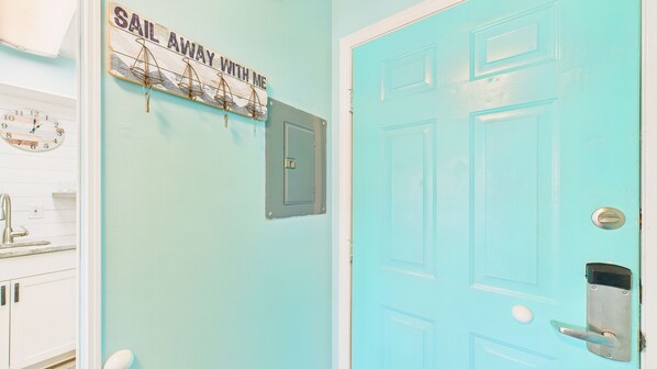 Una habitación con una puerta azul claro, un reloj fijado en la pared y un letrero que dice 'Sail Away With Me'.