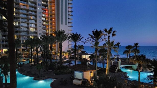 A resort pool area with a view of a tall hotel building and the ocean at dusk. - Lagoon Lookout 811-Gulf-Front Views-Sleeps 6 (Panama City Beach)