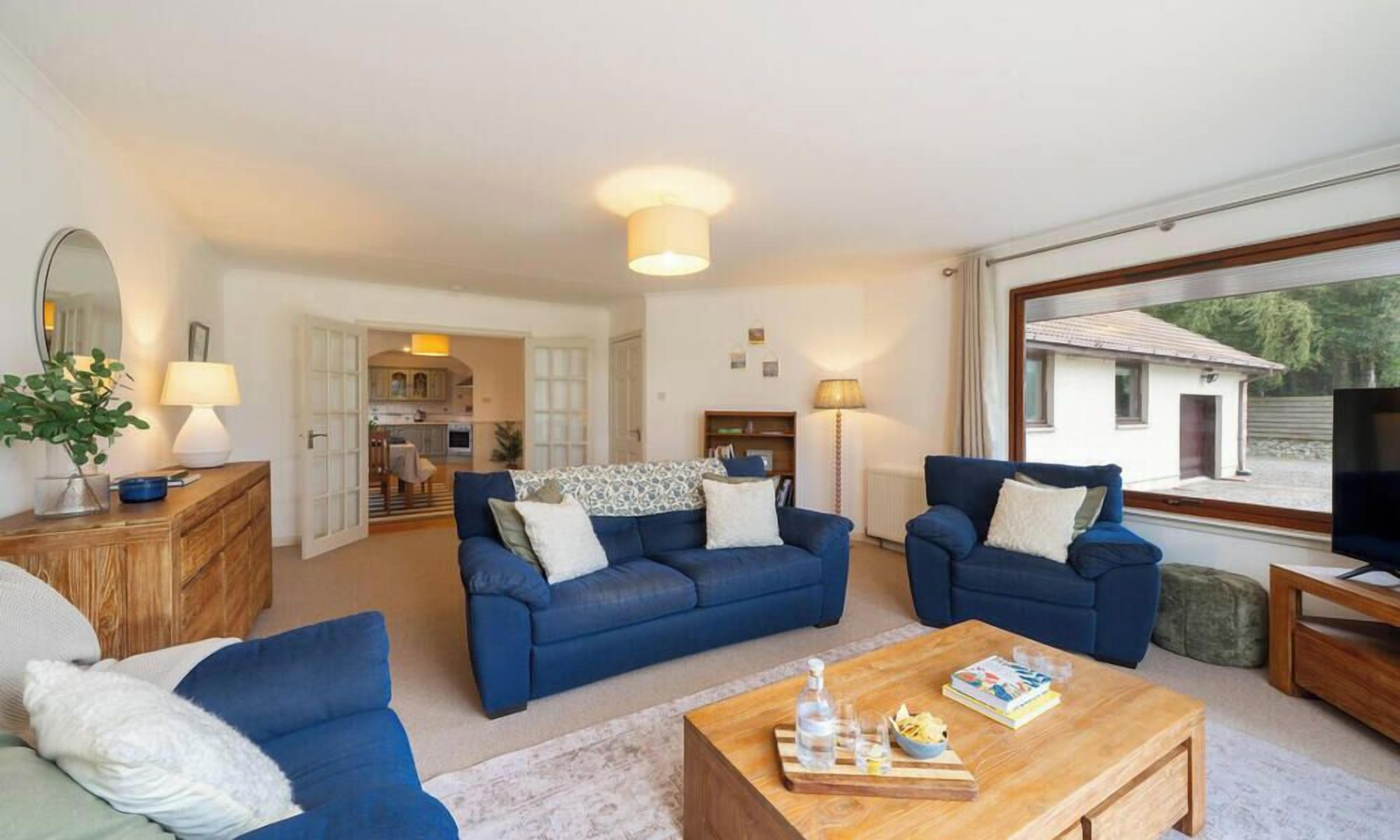 A spacious living room with two blue sofas, a wooden coffee table, and a TV on a wooden stand.