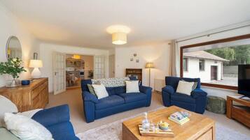A spacious living room with two blue sofas, a wooden coffee table, and a TV on a wooden stand.