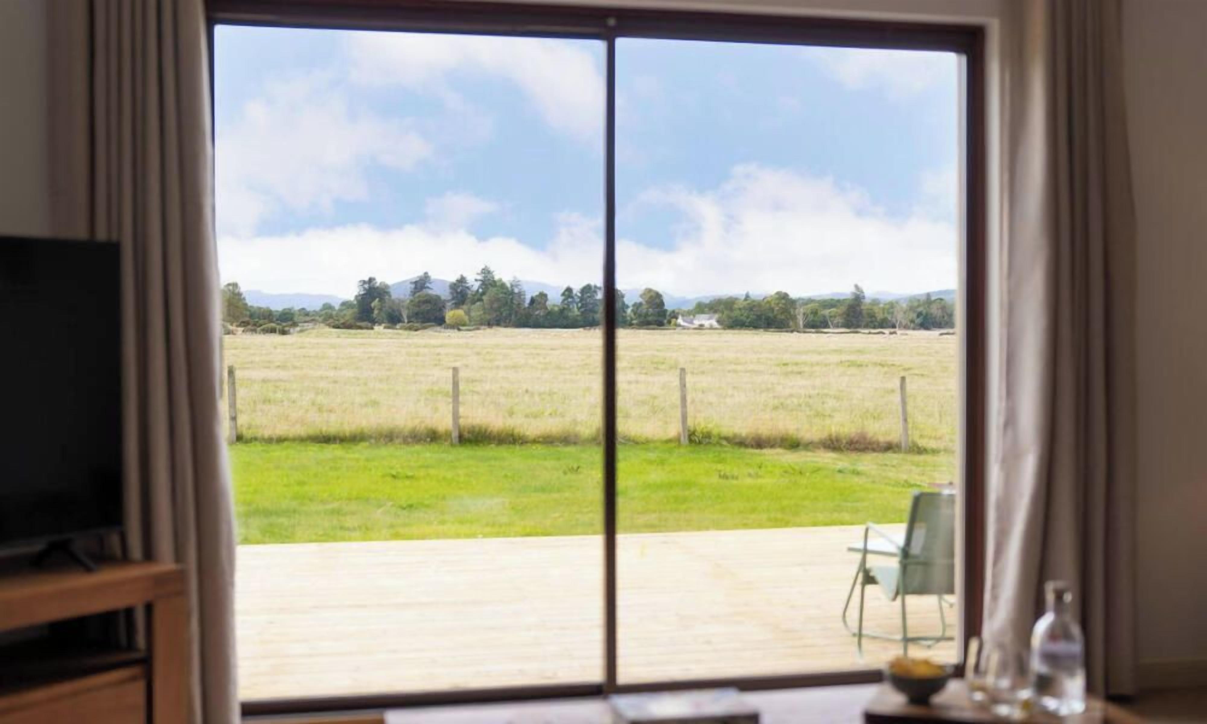 A room with a large sliding glass door leading to an outdoor area with a grassy field and trees.