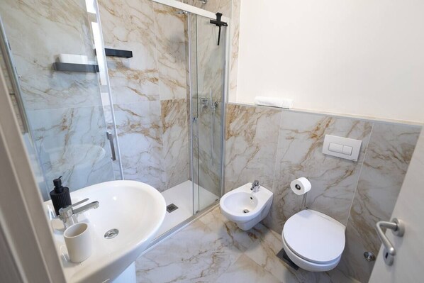Un baño moderno con ducha de vidrio, lavabo blanco, bidé y retrete.