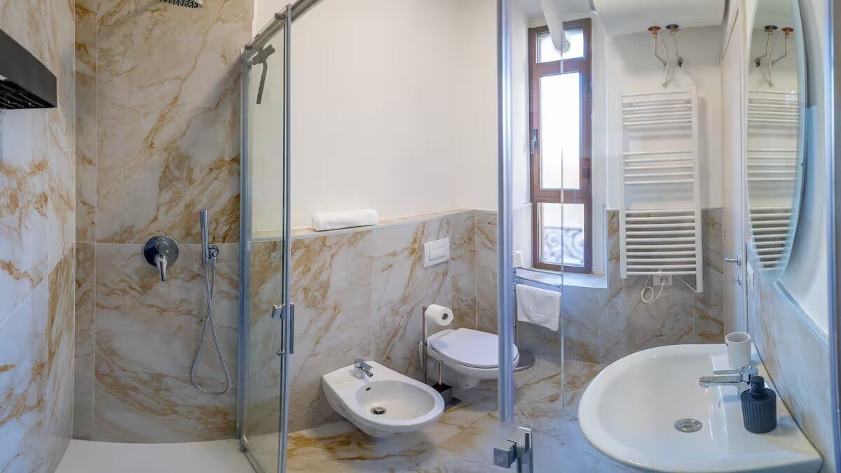 A modern bathroom with a glass-enclosed shower, a bidet, a toilet, and a sink with a mirror.